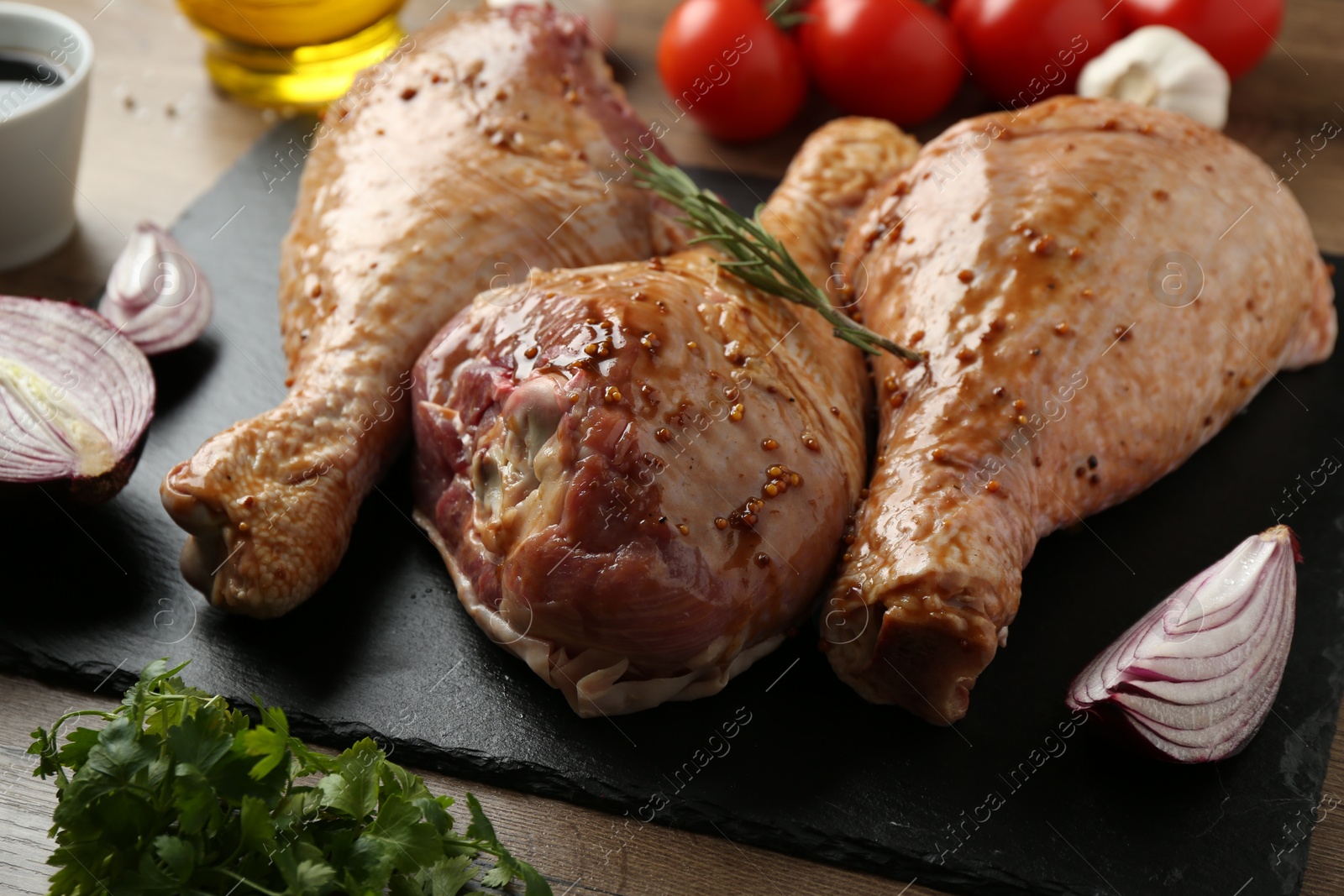 Photo of Raw marinated turkey drumsticks and products on wooden table, closeup