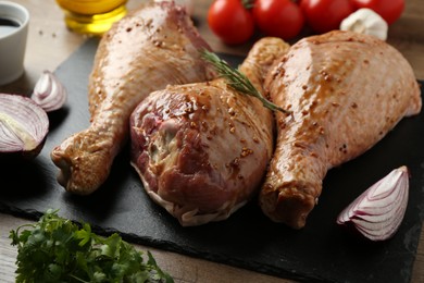 Photo of Raw marinated turkey drumsticks and products on wooden table, closeup