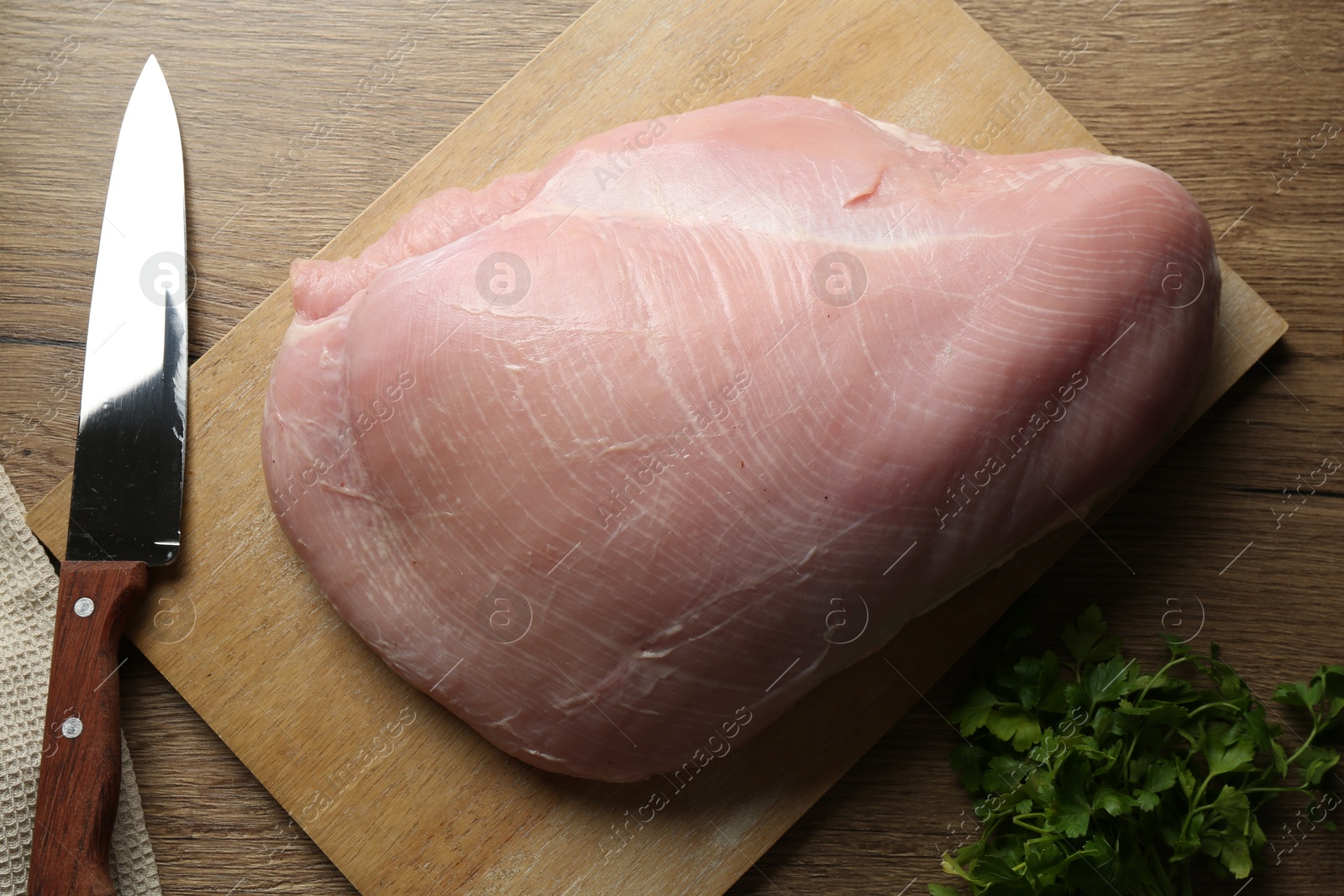 Photo of Piece of raw turkey meat, knife and parsley on wooden table, closeup