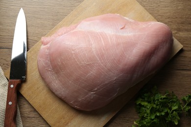 Photo of Piece of raw turkey meat, knife and parsley on wooden table, closeup