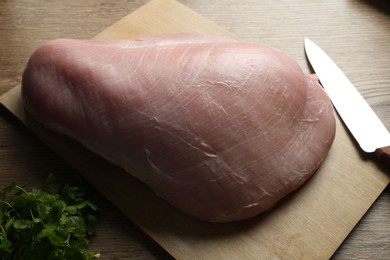 Photo of Piece of raw turkey meat, knife and parsley on wooden table, closeup