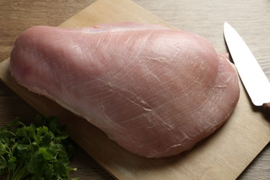 Photo of Piece of raw turkey meat, knife and parsley on wooden table, closeup