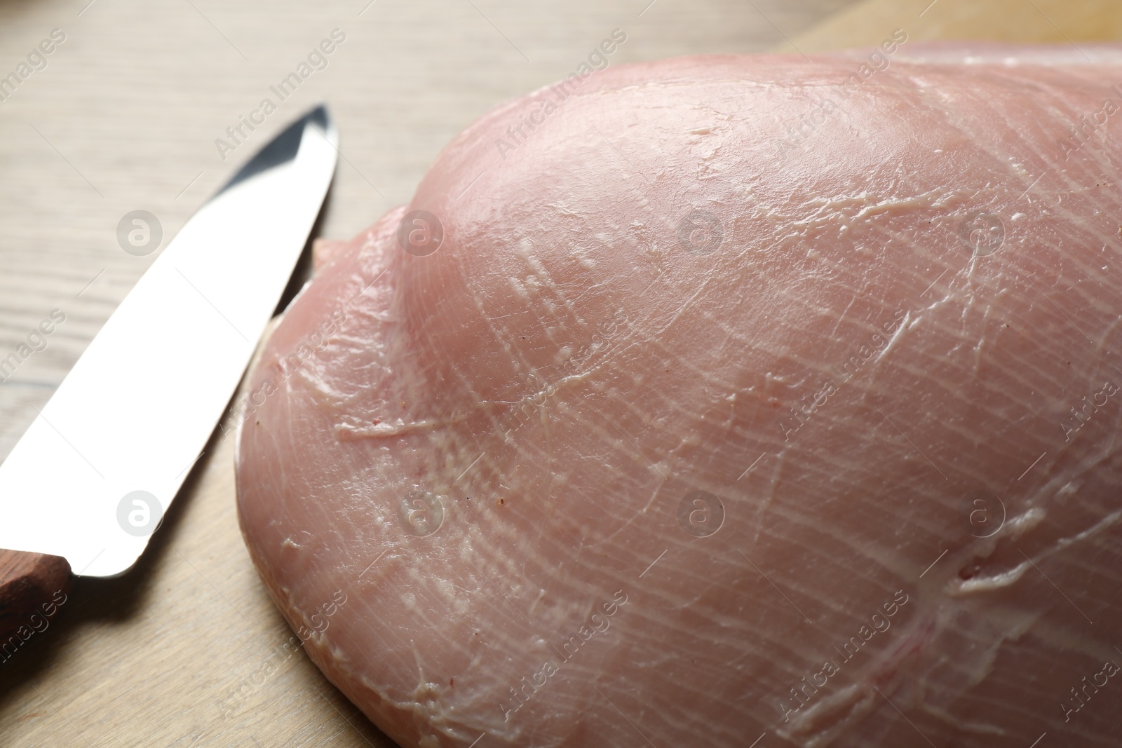 Photo of Piece of raw turkey meat and knife on wooden table, closeup