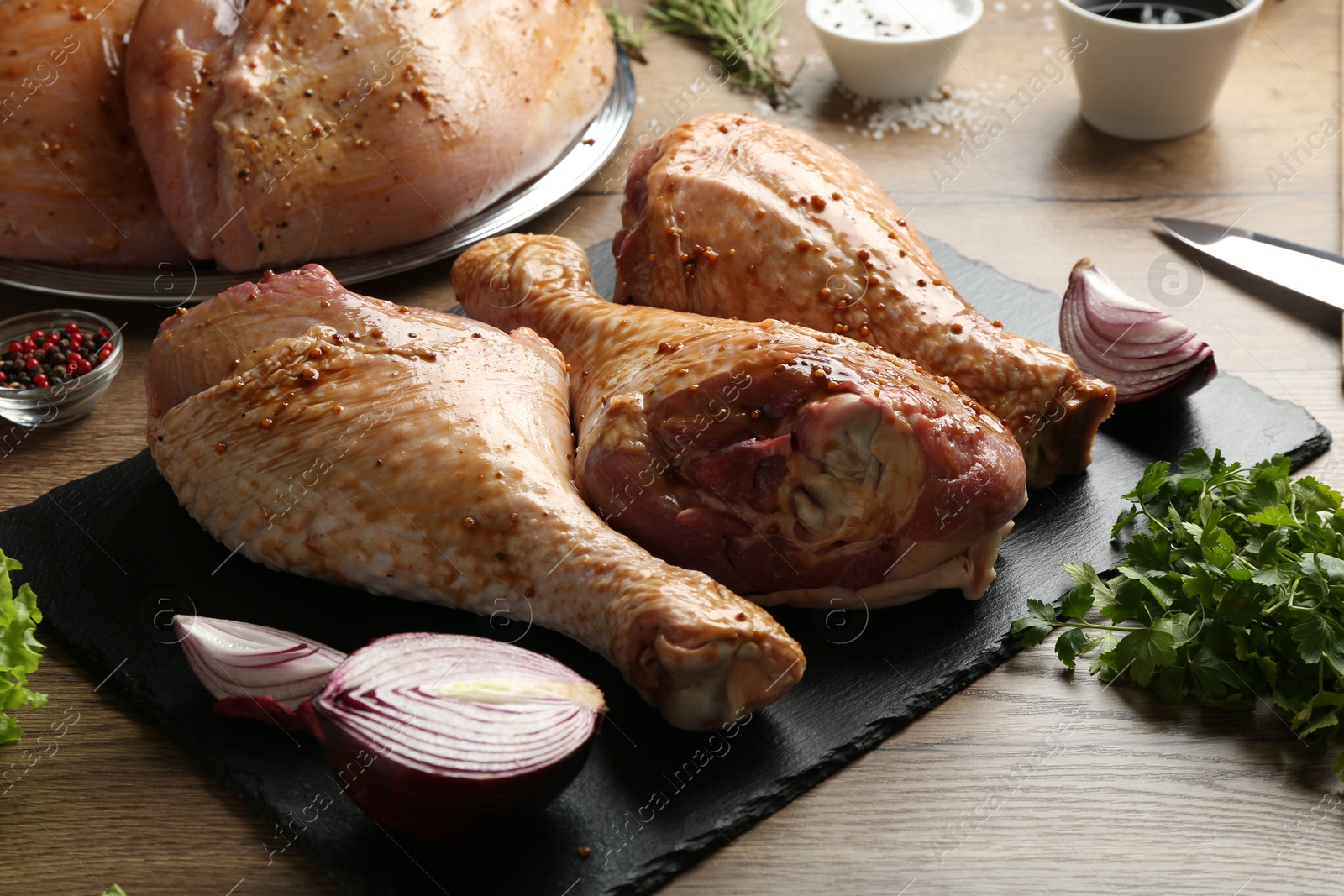 Photo of Raw marinated turkey drumsticks and products on wooden table, closeup