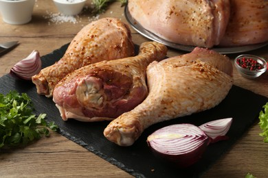 Photo of Raw marinated turkey drumsticks and products on wooden table, closeup