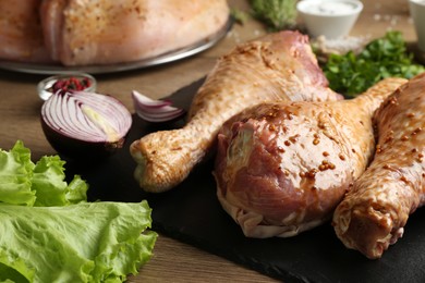 Photo of Raw marinated turkey drumsticks and products on wooden table, closeup