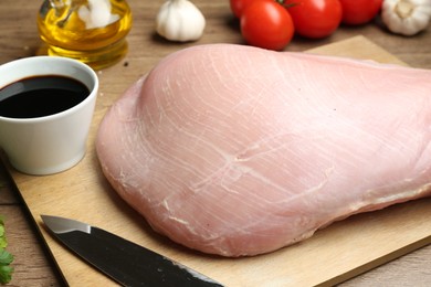 Photo of Raw turkey breast, soy sauce and knife on wooden table, closeup