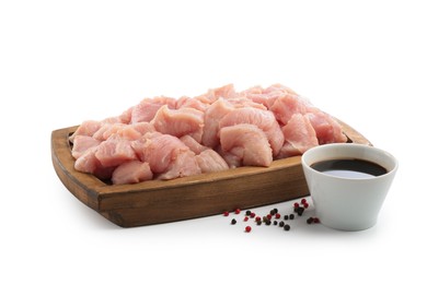 Photo of Wooden board with pieces of raw turkey meat, soy sauce and peppercorns isolated on white