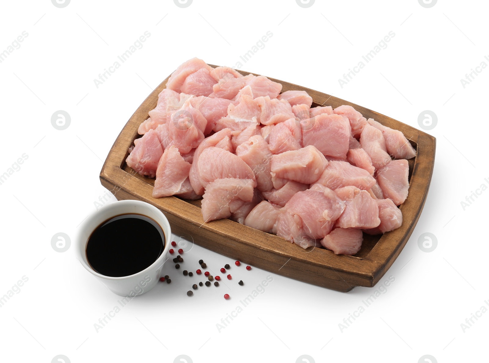 Photo of Wooden board with pieces of raw turkey meat, soy sauce and peppercorns isolated on white