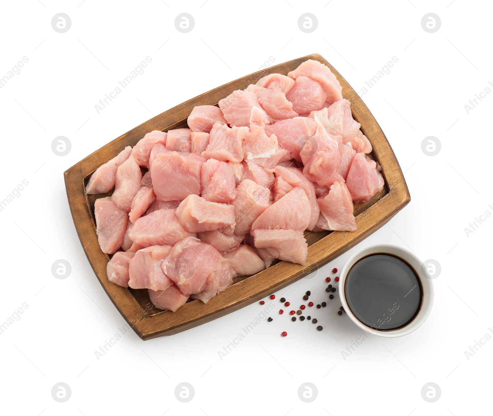 Photo of Wooden board with pieces of raw turkey meat, soy sauce and peppercorns isolated on white, top view