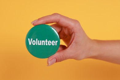 Photo of Woman showing green button badge with word Volunteer on orange background, closeup