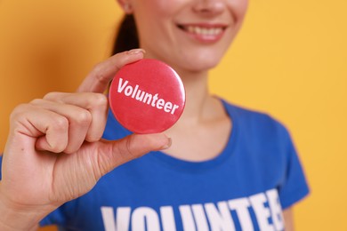 Woman showing red button badge with word Volunteer on orange background, closeup