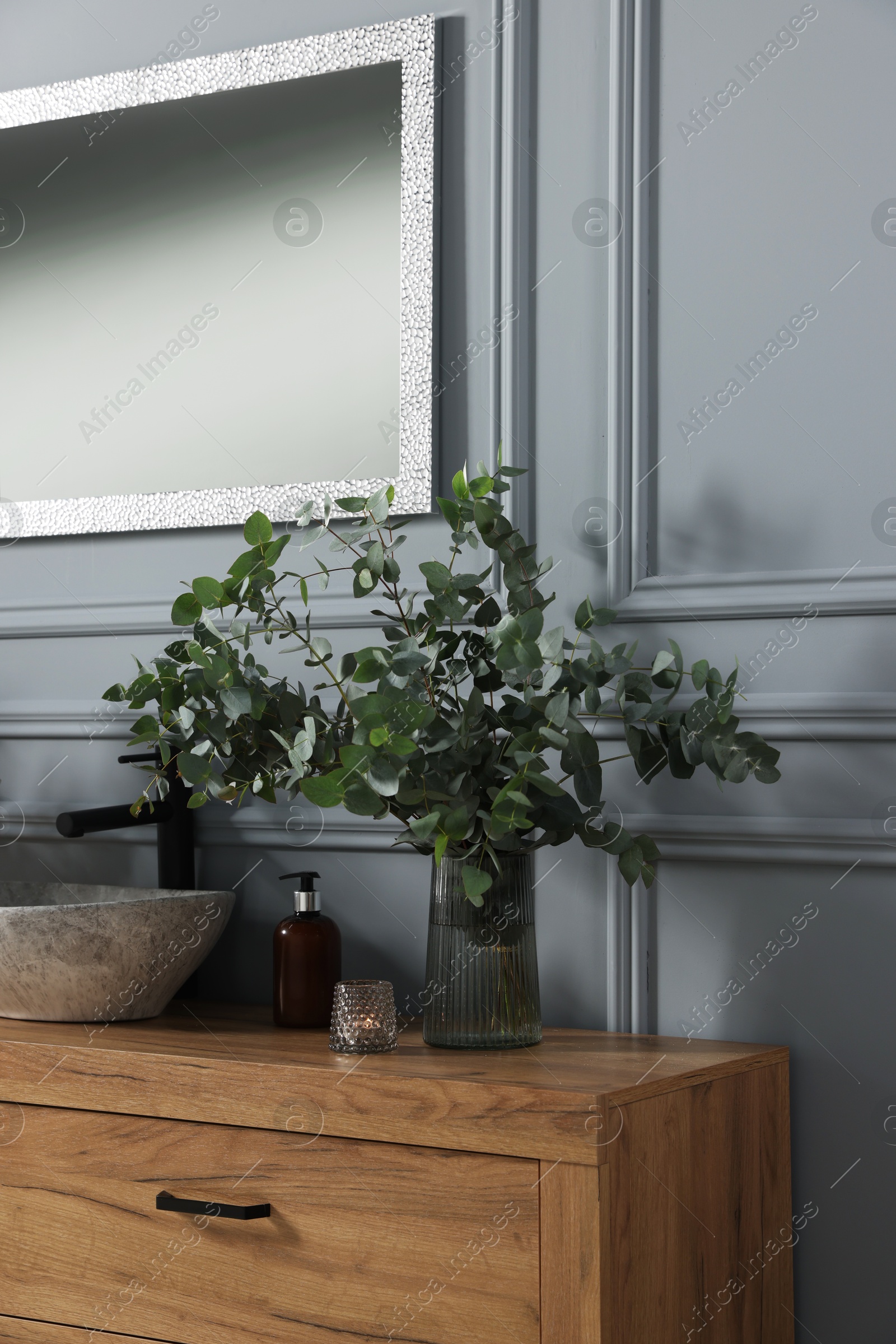 Photo of Eucalyptus branches and candle near vessel sink on bathroom vanity. Interior design