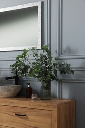 Photo of Eucalyptus branches and candle near vessel sink on bathroom vanity. Interior design