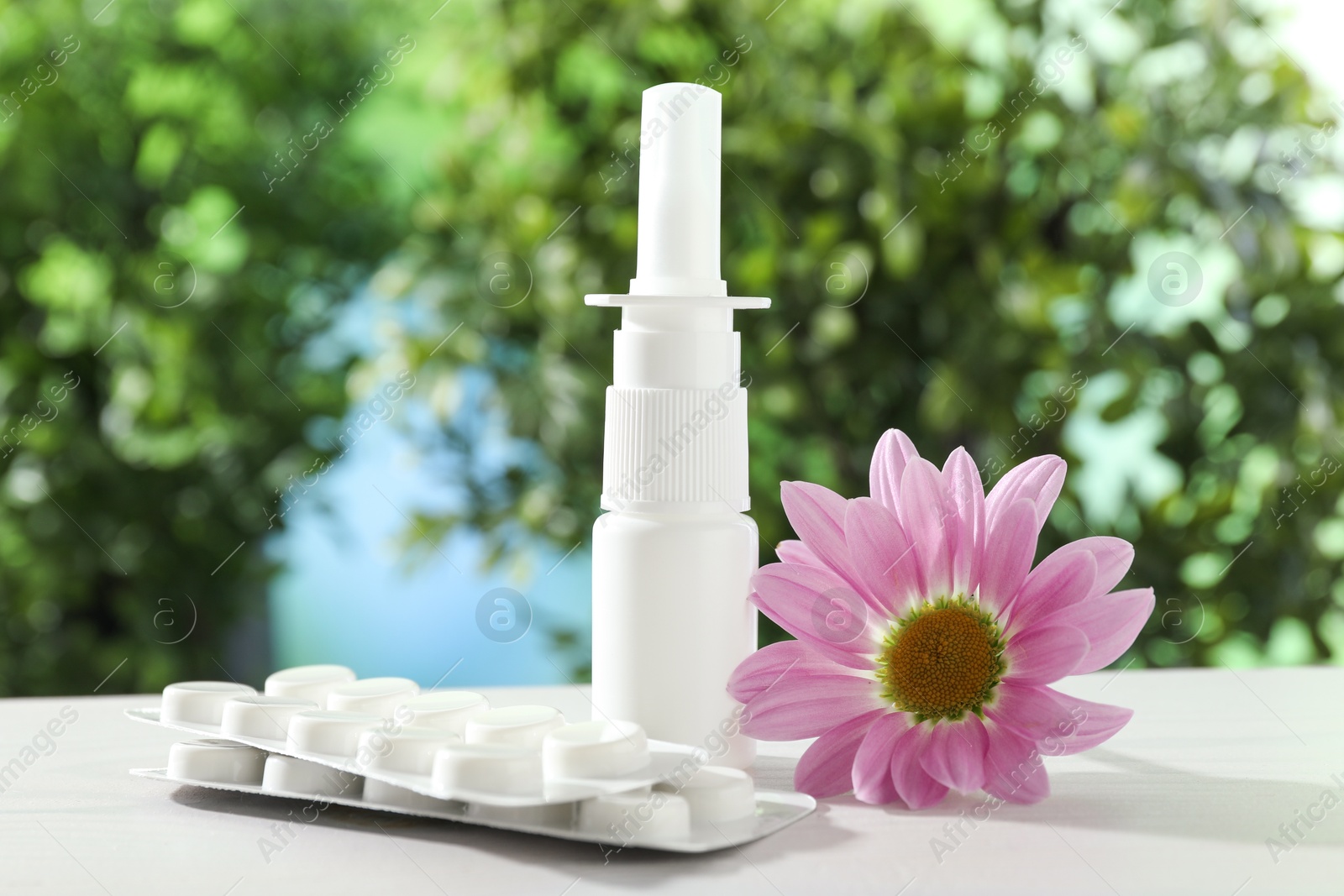 Photo of Allergy treatment. Nasal spray, pills and flower on white table against blurred background