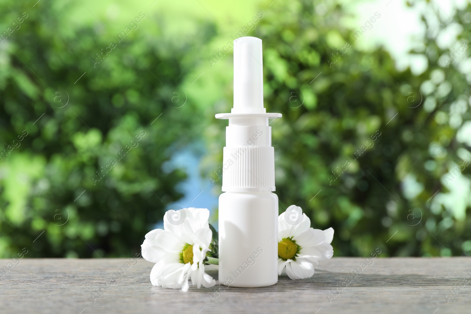 Photo of Allergy treatment. Nasal spray and flowers on wooden table against blurred background