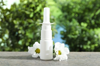 Photo of Allergy treatment. Nasal spray and flowers on wooden table against blurred background