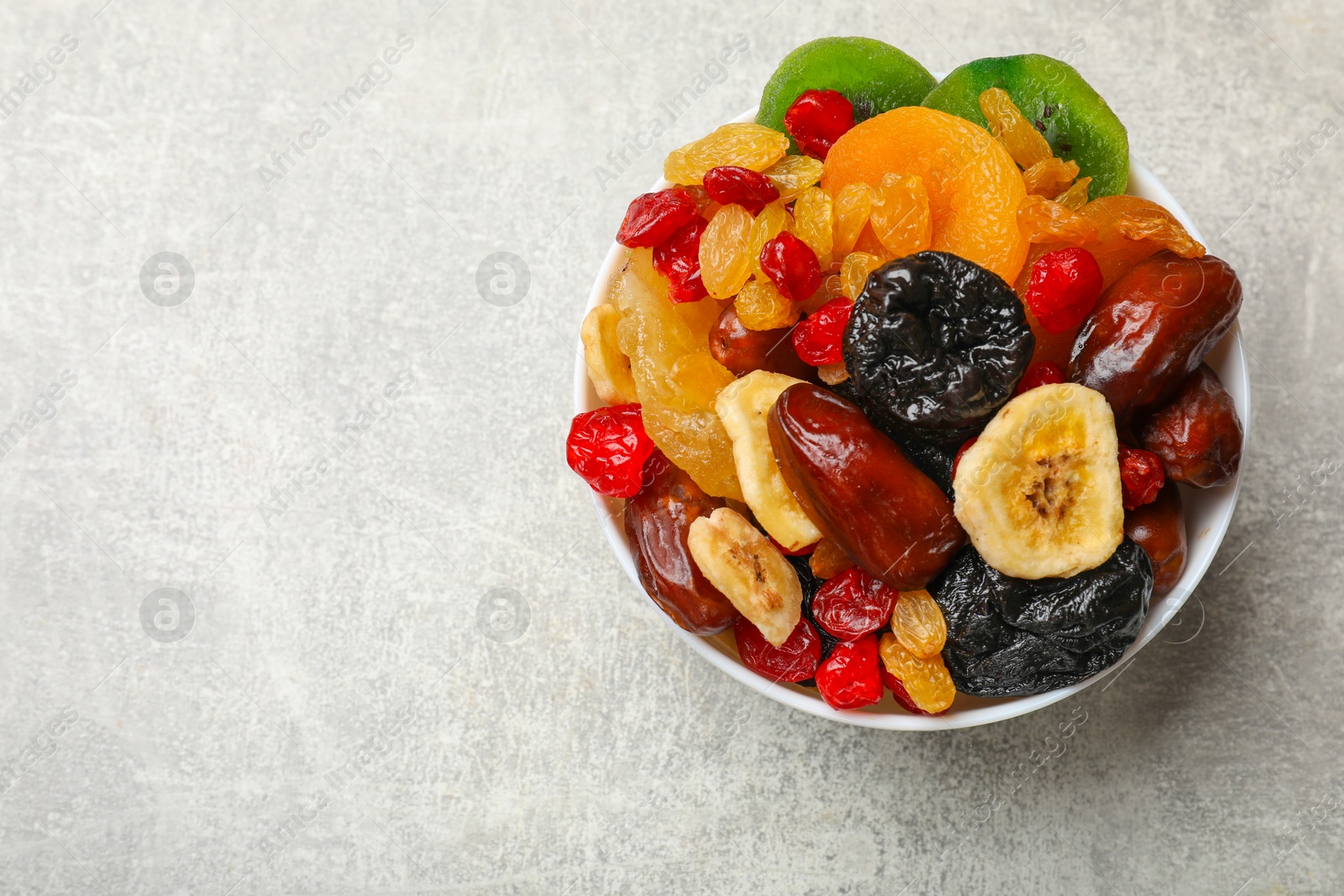 Photo of Mix of different dried fruits in bowl on grey table, top view. Space for text