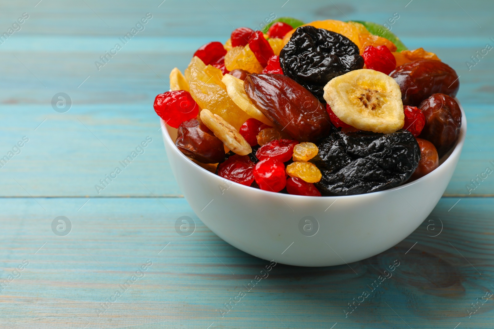 Photo of Mix of different dried fruits in bowl on blue wooden table, closeup