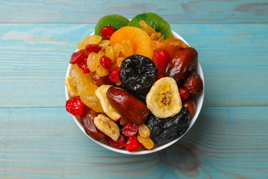 Photo of Mix of different dried fruits in bowl on blue wooden table, top view