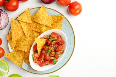 Photo of Delicious salsa (Pico de gallo) served with nachos and products on white wooden table, flat lay. Space for text