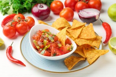 Photo of Delicious salsa (Pico de gallo) served with nachos and ingredients on white wooden table, closeup