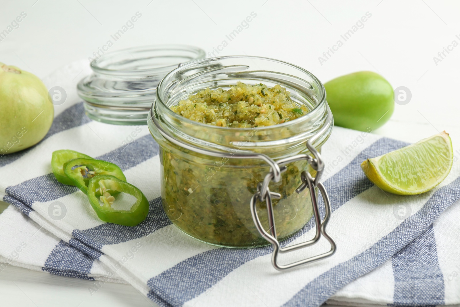 Photo of Delicious salsa sauce in jar and products on white table, closeup