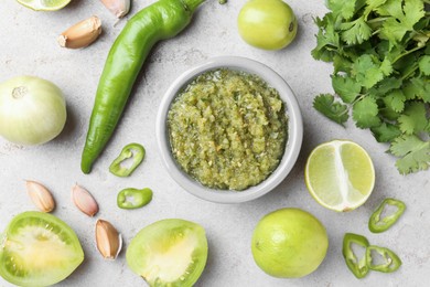 Photo of Delicious salsa sauce in bowl and ingredients on light textured table, flat lay