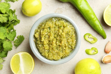 Photo of Delicious salsa sauce in bowl and ingredients on light textured table, flat lay