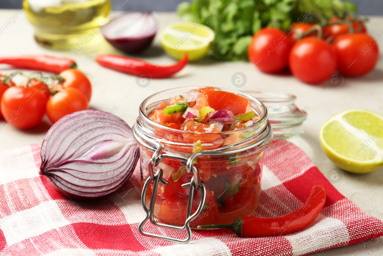 Photo of Delicious salsa (Pico de gallo) in jar and ingredients on light table, closeup