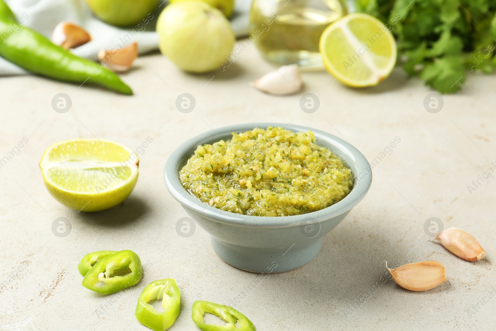 Photo of Delicious salsa sauce in bowl and products on light textured table, closeup