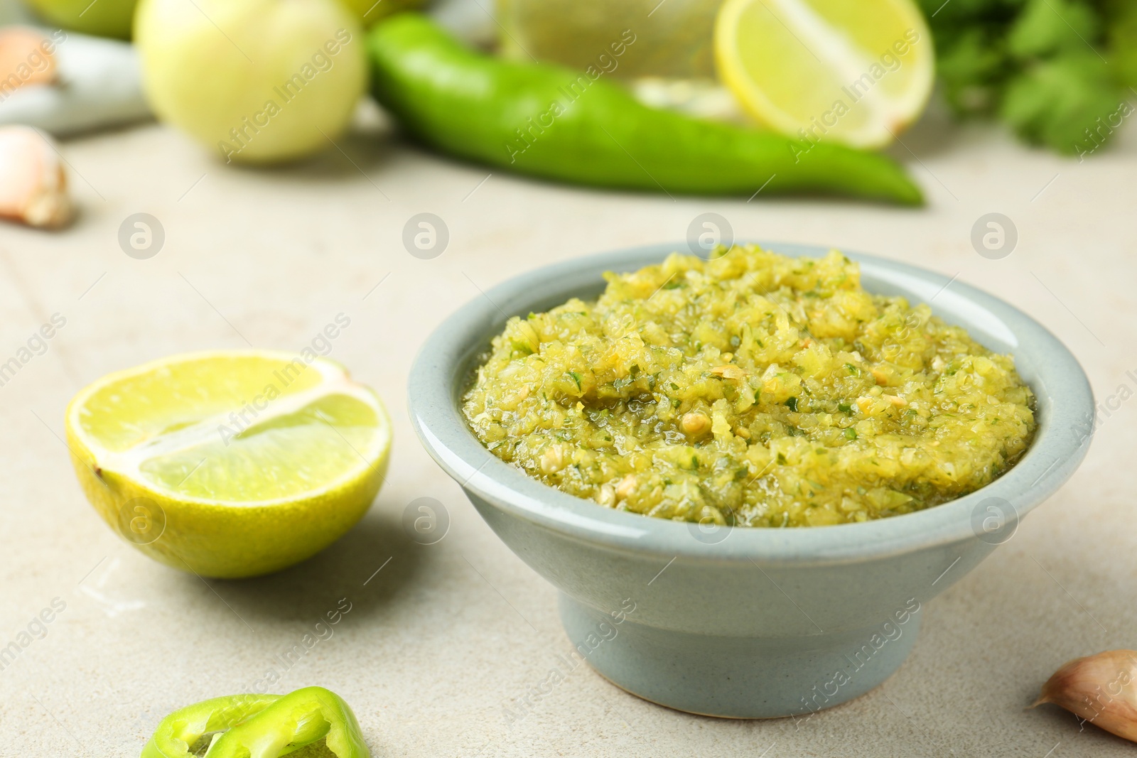 Photo of Delicious salsa sauce in bowl and products on light textured table, closeup