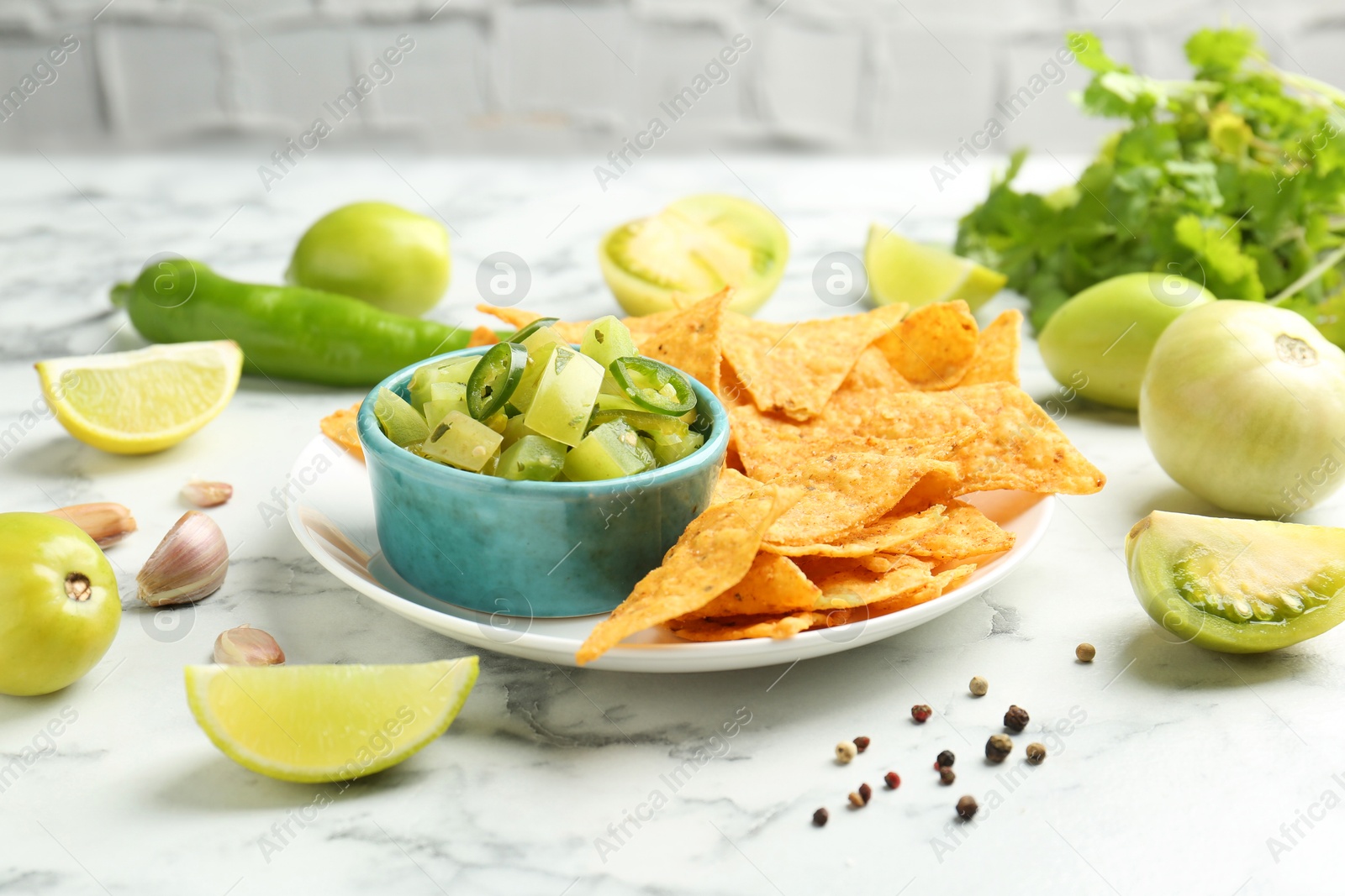 Photo of Delicious salsa with nachos on white marble table