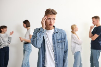 Photo of Young man feeling uncomfortable among people indoors, selective focus