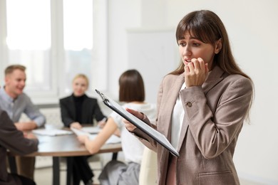 Photo of Glossophobia. Woman with clipboard feeling embarrassed during business meeting in office, selective focus