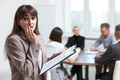 Photo of Glossophobia. Woman with clipboard feeling embarrassed during business meeting in office, selective focus