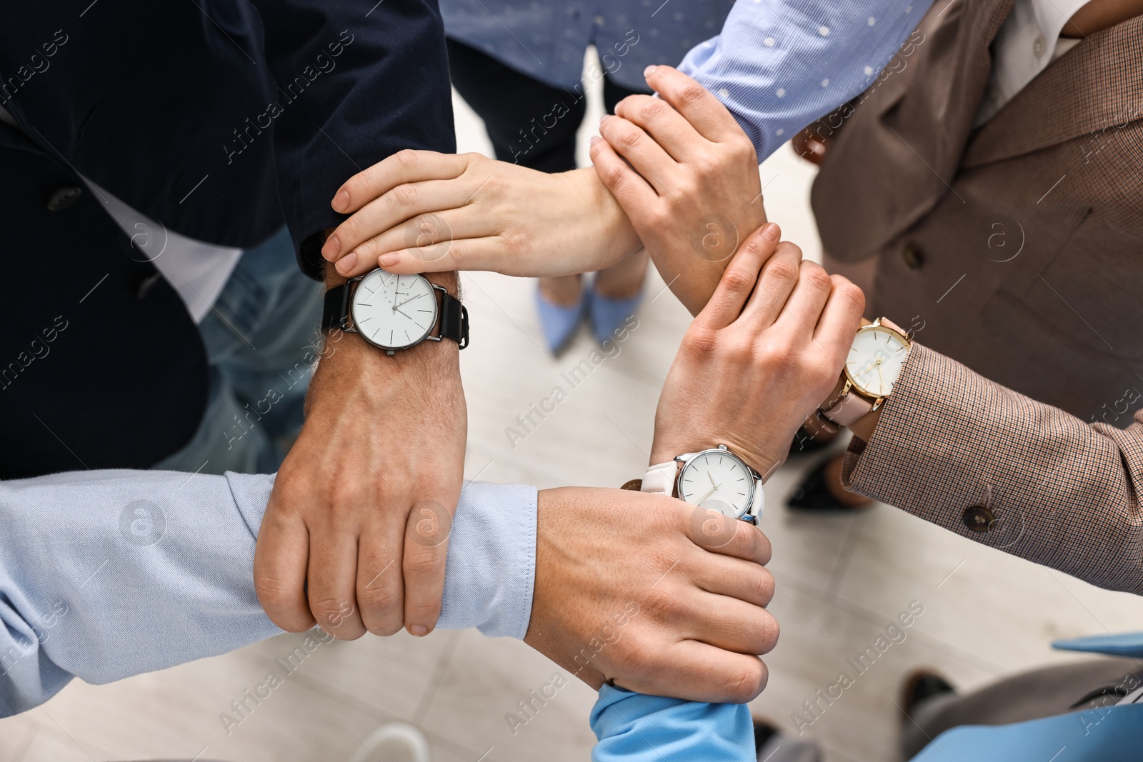 Photo of Teamwork. Group of people holding hands together indoors, top view