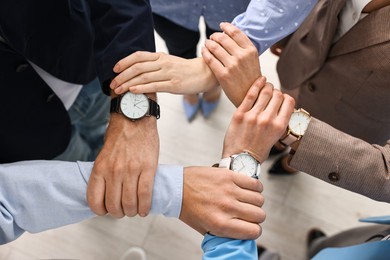 Photo of Teamwork. Group of people holding hands together indoors, top view