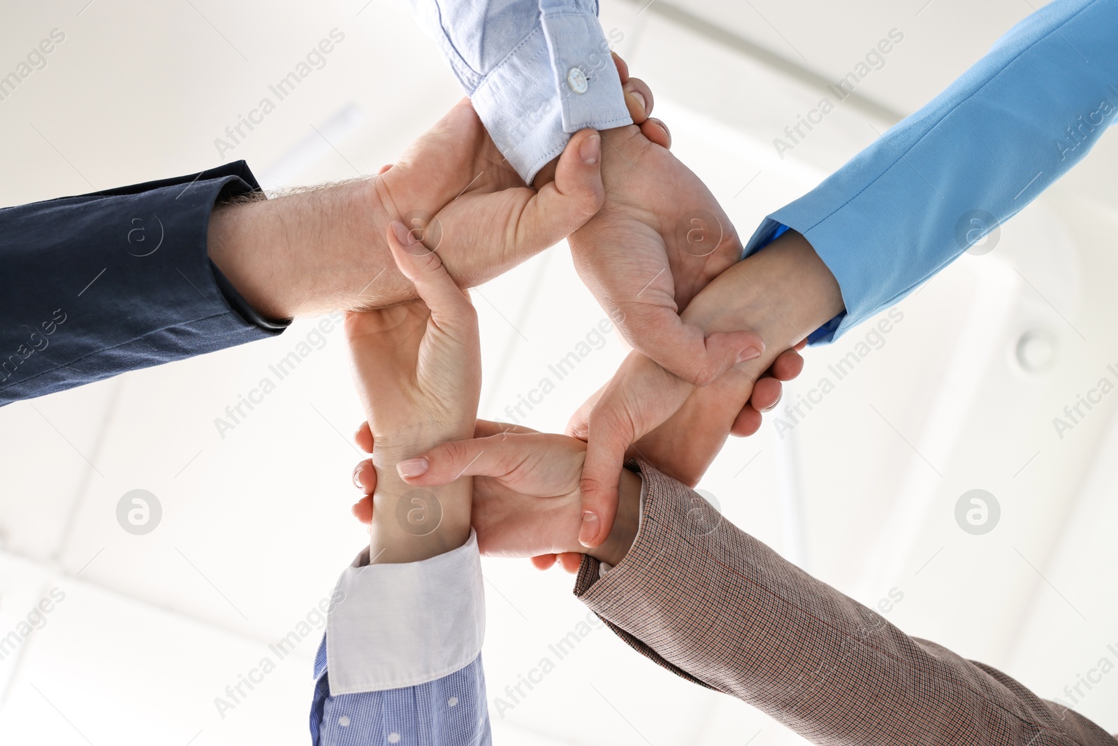 Photo of Teamwork. Group of people holding hands together indoors, bottom view