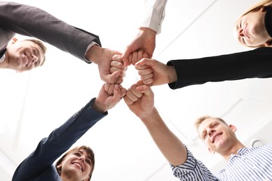 Teamwork. Group of people joining fists together indoors, bottom view