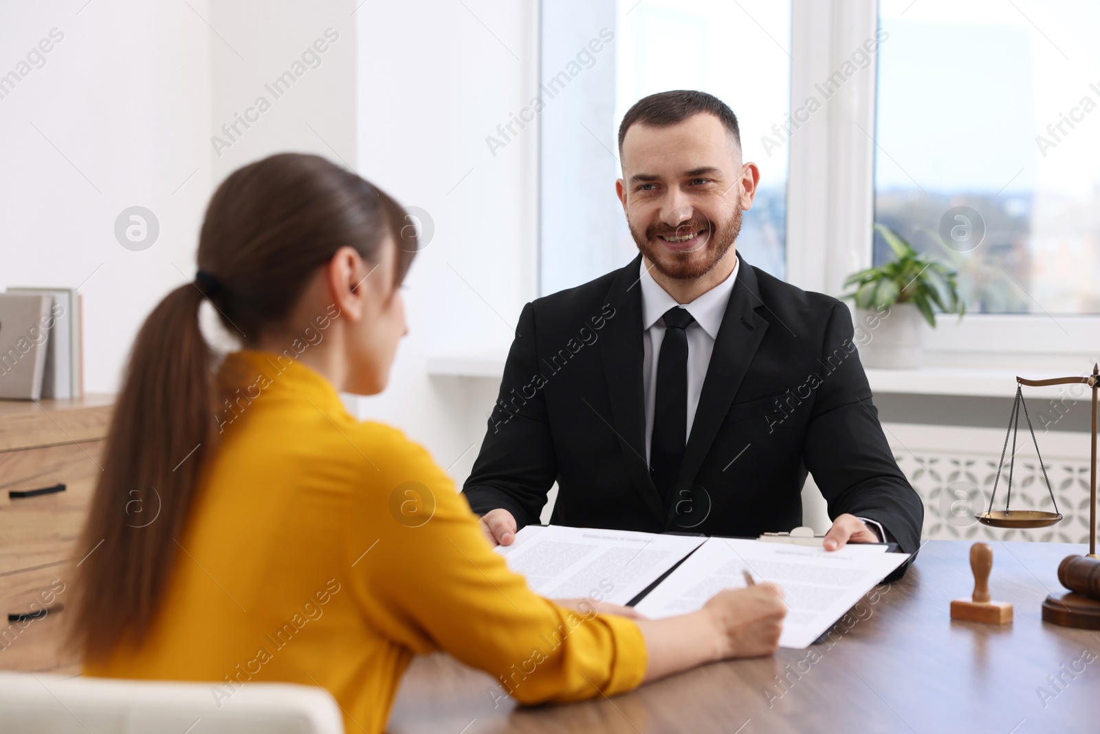 Photo of Client signing notarial paperwork during meeting with lawyer at wooden desk indoors