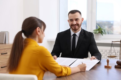 Photo of Client signing notarial paperwork during meeting with lawyer at wooden desk indoors