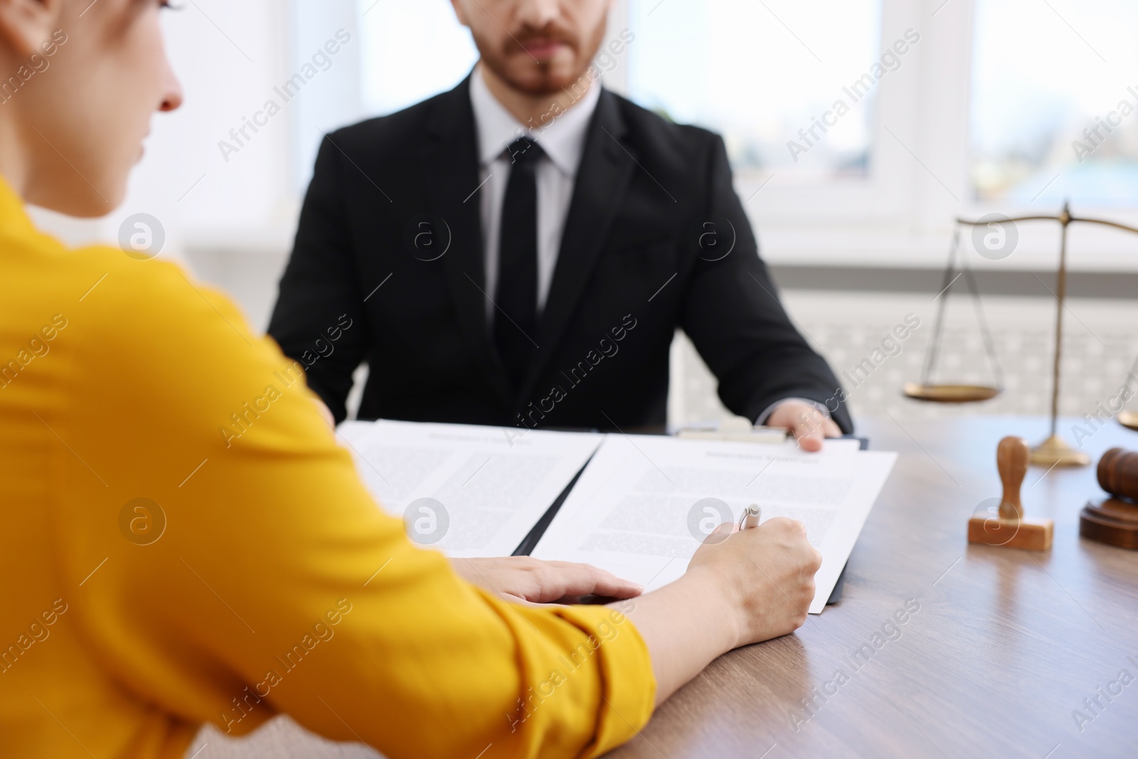 Photo of Client signing notarial paperwork during meeting with lawyer at wooden desk indoors, closeup