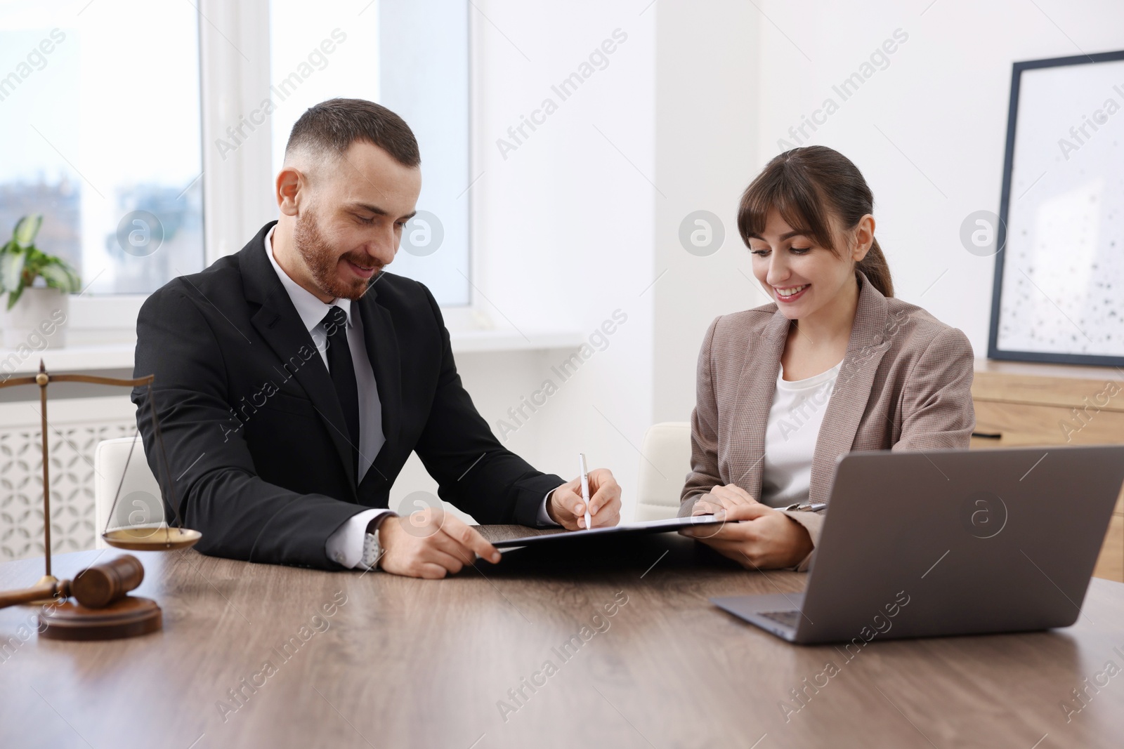 Photo of Client signing notarial paperwork during meeting with lawyer at wooden desk indoors