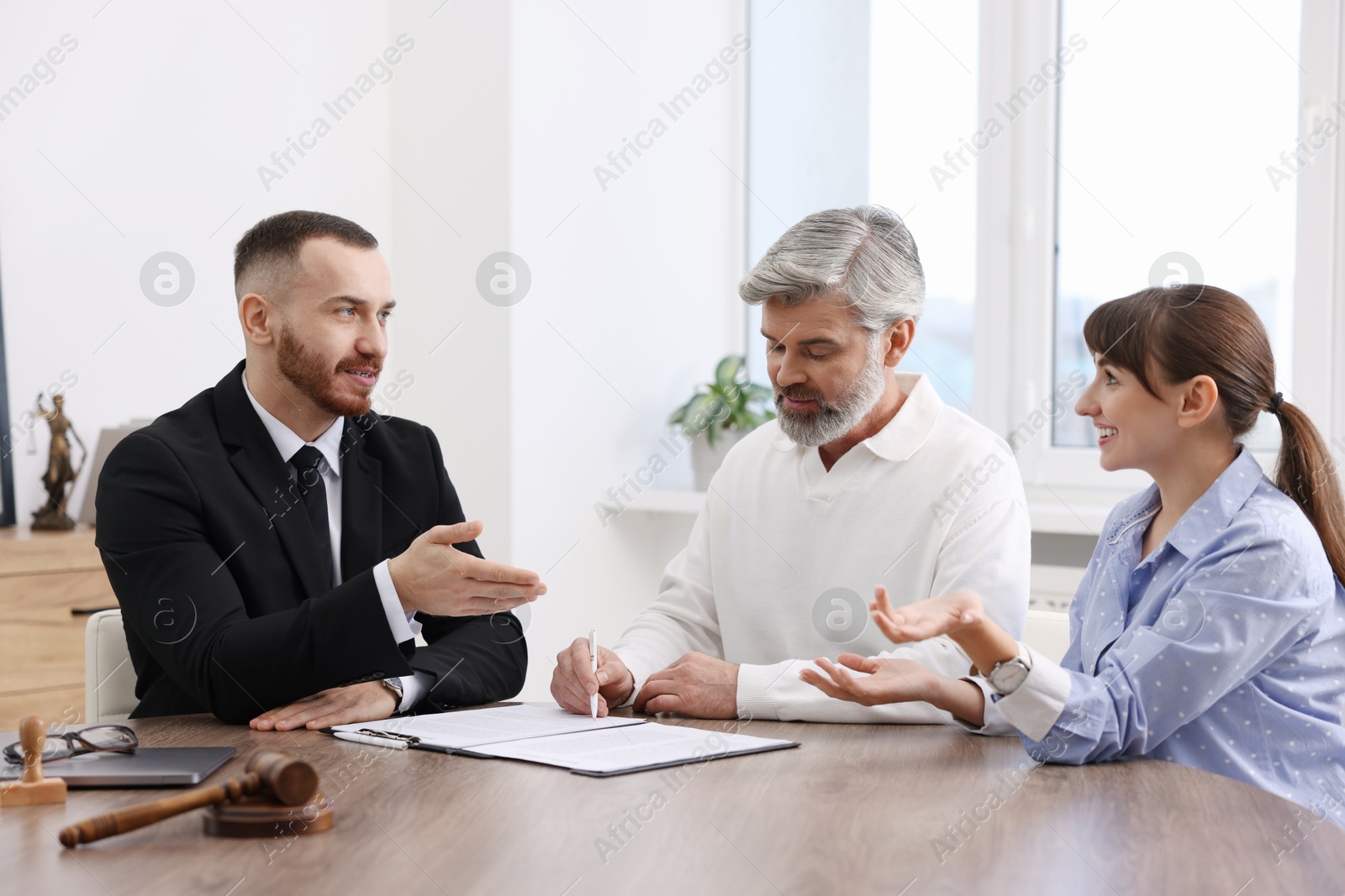 Photo of Couple having meeting with professional notary at wooden desk indoors