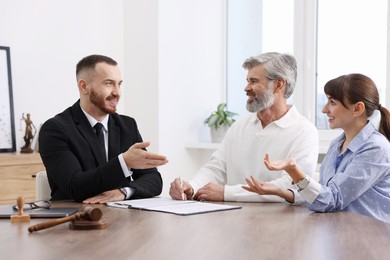 Photo of Couple having meeting with professional notary at wooden desk indoors