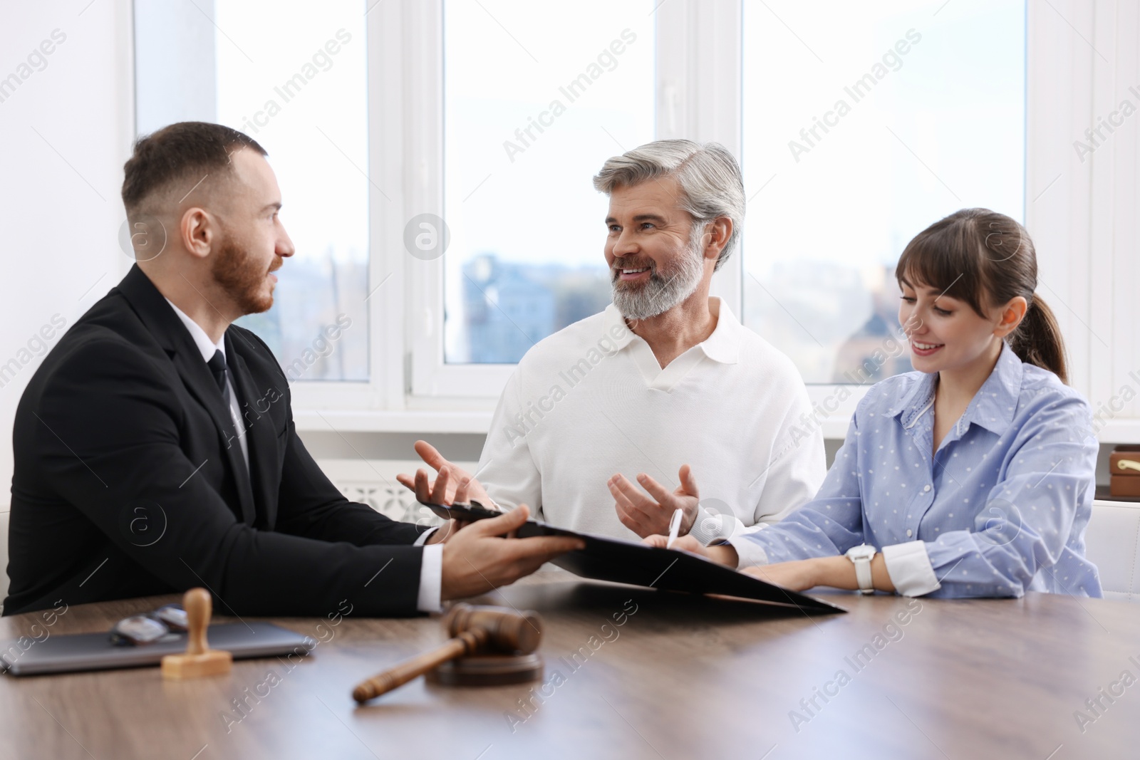 Photo of Clients signing notarial paperwork during meeting with lawyer at wooden desk indoors