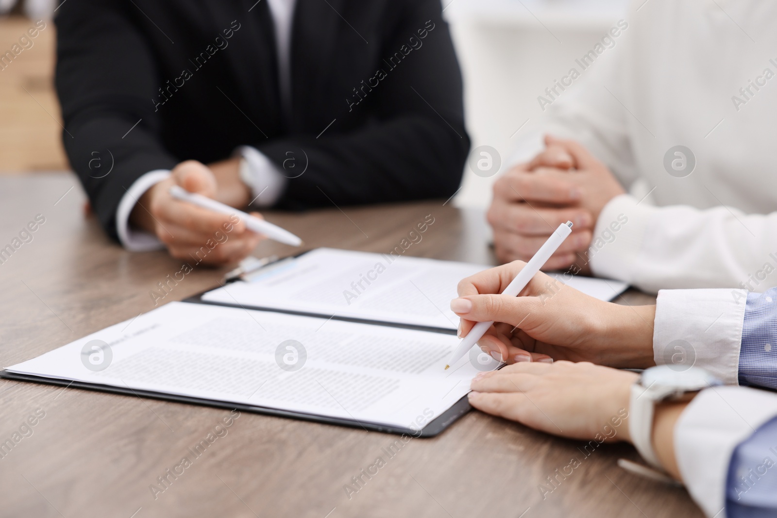 Photo of Clients signing notarial paperwork during meeting with lawyer at wooden desk indoors, closeup