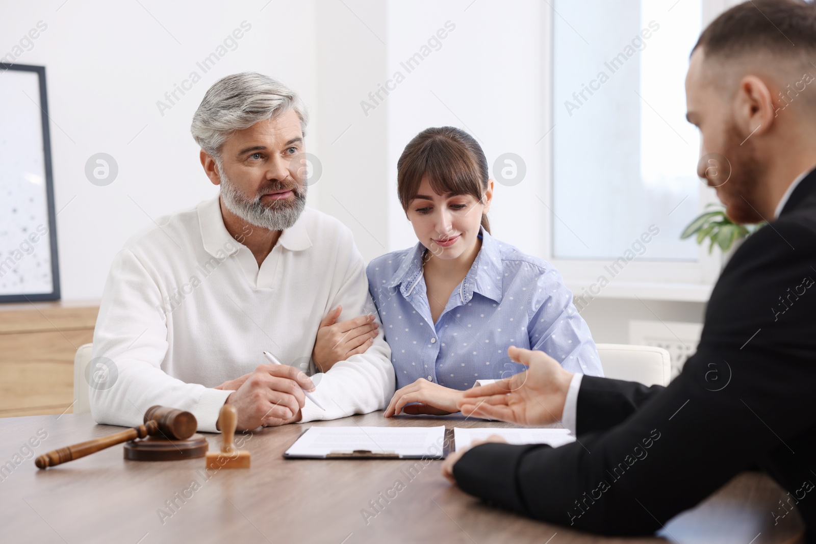 Photo of Couple having meeting with professional notary at wooden desk indoors