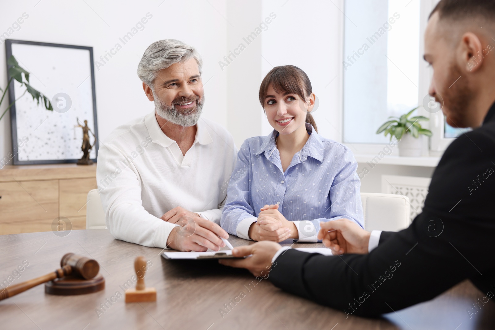 Photo of Clients signing notarial paperwork during meeting with lawyer at wooden desk indoors